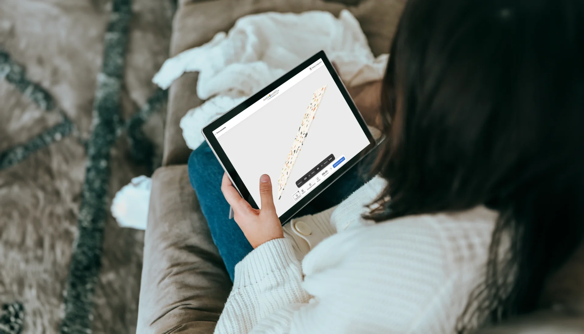 Donna seduta su un divano che utilizza un tablet per configurare un prodotto in marmo/granito tramite il visualizzatore 3D MarmoGranito.